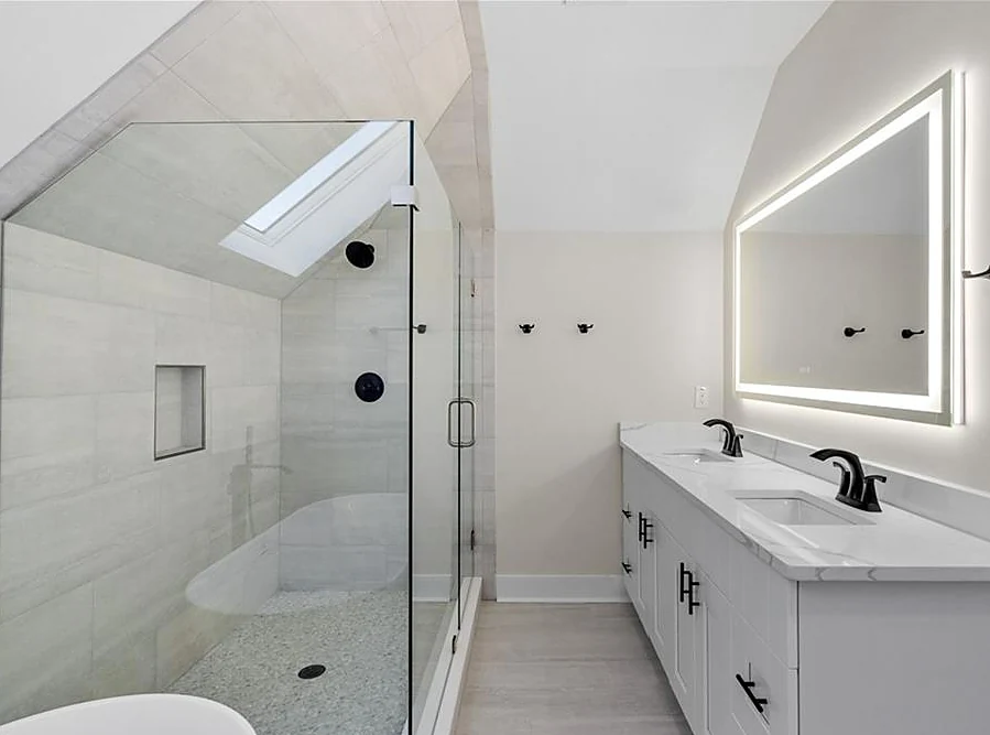 Primary bathroom with a skylit walk-in glass shower, freestanding tub, double vanity and backlit mirror