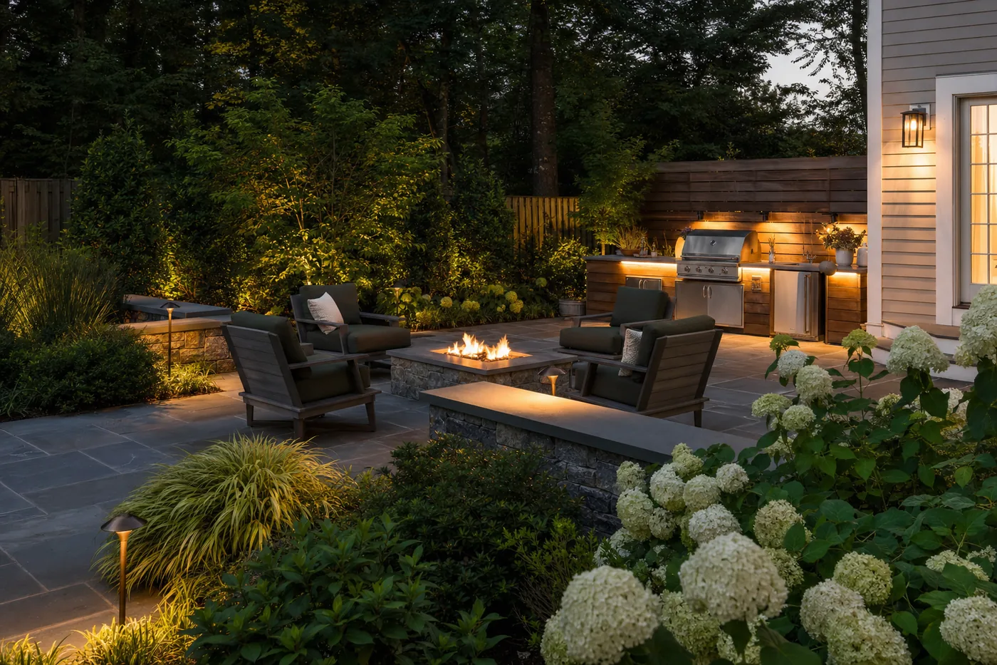 Bluestone patio with fire pit, outdoor kitchen and landscape lighting at dusk